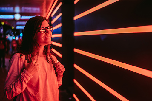 Young smiling woman with eyeglasses, standing in front of orange neon lights. Hamburg, Germany.