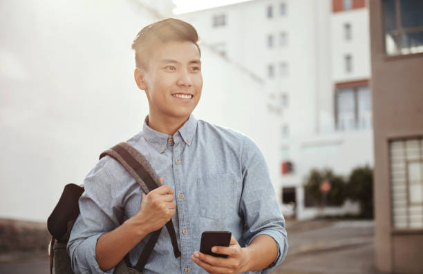 Today college, tomorrow a career Shot of a happy young student using his smartphone in the city male chinese student stock pictures, royalty-free photos & images