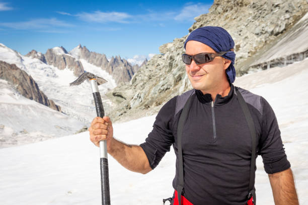 Smiling alpinist mountaineer posing holding ice axe, Chamonix, France mountains Alps background.