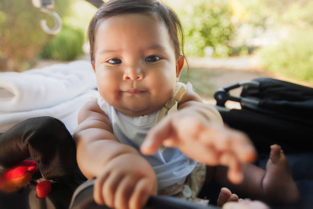 istock A cute baby using her hands to reach for something infront of her while riding on a carriage type of stroller. 1157213703
