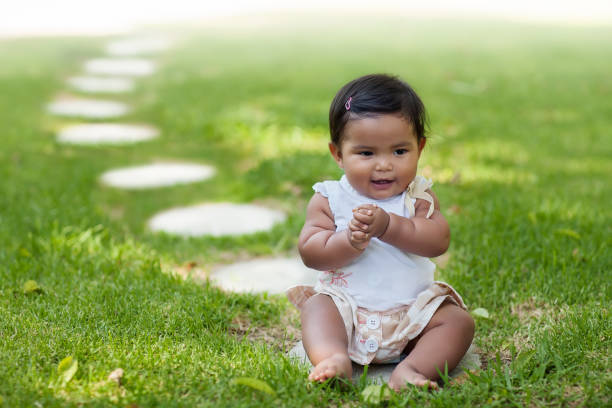 istock A baby girl grasping her own hands while sitting on the frontmost stepping stone from a series of stepping stones that go into perspective. 1157213717