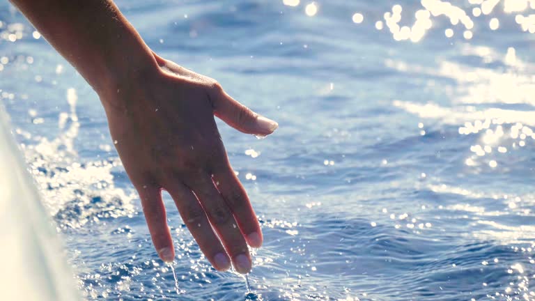 an young womanl on a boat touches the water and enjoys the day at the sea alongside the waves of the boat.