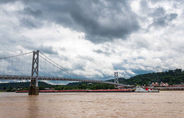 istock Barge Pushing Coal Containers Passing Under an Old Suspension Bridge 1157243312
