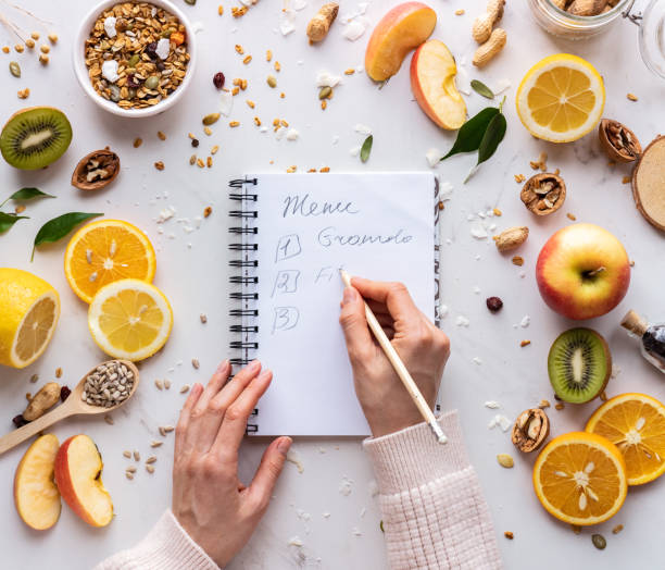 nutritionist female hand write in notebook on healthy food background, women diet nutrition recipe menu, fresh summer fruit granola seeds on white table organic super food health care detox, top view - weight apple loss weightloss imagens e fotografias de stock