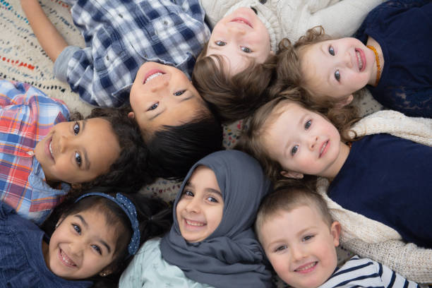 Kids Group Photo A multi-ethnic group of kids is laying on the carpet of their preschool classroom. They are smiling up at the camera while posing for a picture. montessori stock pictures, royalty-free photos & images