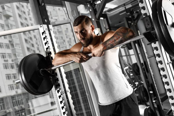 istock Bodybuilding. Bearded man standing leaning on barbell at gym looking forward sassy 1157244746