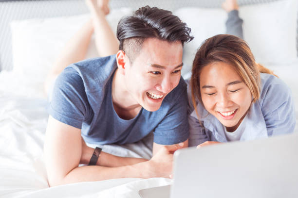 istock Happy Asian couple lying on the bed and using a laptop 1157245768