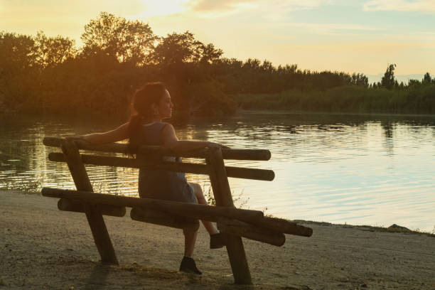 Young brunette woman watching the sunset, sitting on a wooden bench in front of a Tajo river, Spain