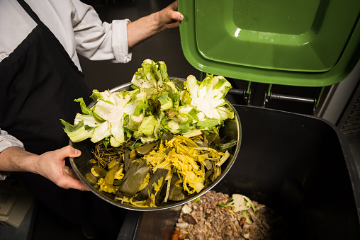 Chef emptying vegetable scraps into a composting bin