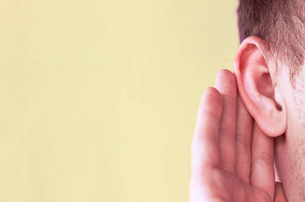 man listens attentively with her palm to her ear, close up, news concept - attentively imagens e fotografias de stock