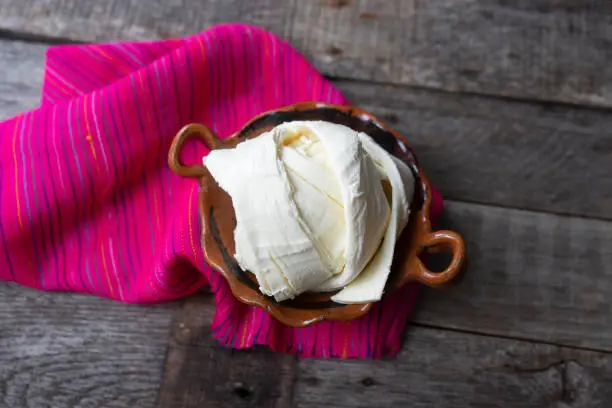 Fresh Oaxaca cheese in clay pot on old wood background