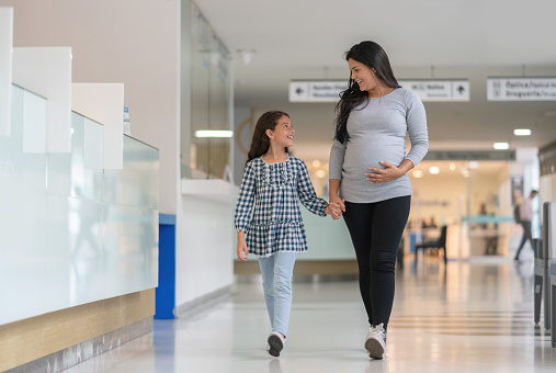 Happy pregnant mother walking with her daughter at the hospital and smiling - healthcare and medicine concepts