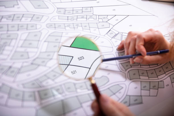istock Human Hand Holding Magnifying Glass Over Cadastre Map 1157269236