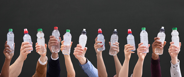 Group Of Different People Holding Water Bottles In A Row Against Green Background