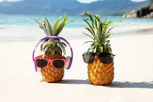 Close-up Of Pineapple With Headphone And Sunglasses On Sand At Beach