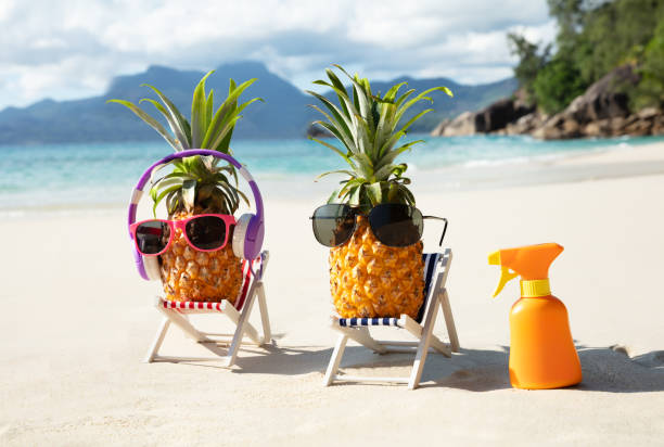 Close-up Of Sunglasses Over Pineapple On Deck Chair Listening Music On Headphone At Beach