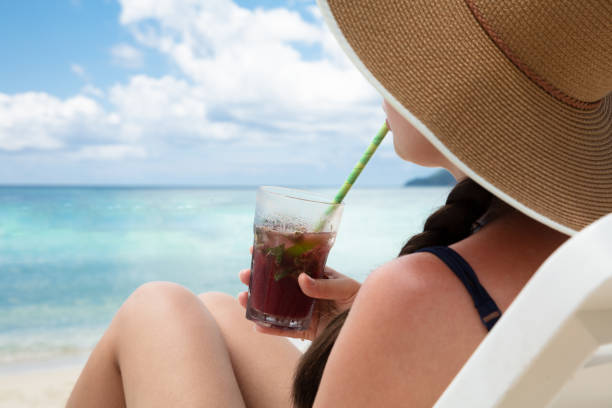istock Woman Wearing Hat Drinking The Juice With Straw On Beach 1157271330