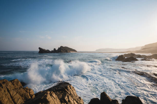 waves crashing on rocky coastline against sky late afternoon - travel destinations rocky coastline moody sky clear sky imagens e fotografias de stock