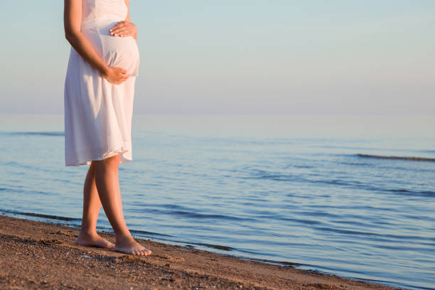 pregnant woman walking at sea beach. touching belly with hands. sunset light. emotional pregnancy time. baby expectation. empty place for lovely, inspiration, sentimental text, quote or cute sayings. - dress human pregnancy young women women imagens e fotografias de stock