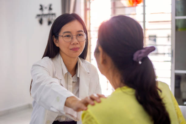 asiatische ärztin tröstet patientin zu hause - geduld stock-fotos und bilder