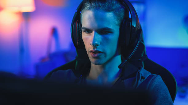 istock Gamer in Headset with a Mic Playing Online Video Game on His Personal Computer. He is Focused on Monitor. Room and Personal Computer have Blue Neon Led Lights. Cozy Evening at Home. 1157289656