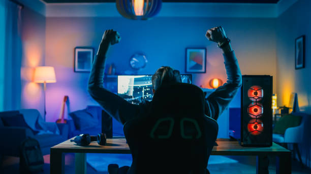 retour shot of a gamer playing and winning in first-person shooter online video game on his powerful personal computer. chambre et pc ont colorful neon led lights. soirée douillette à la maison. - gamer photos et images de collection