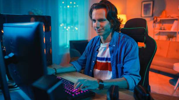 Excited Gamer Playing Online Video Game on His Personal Computer. Room and Personal Computer have Colorful Warm Neon Led Lights. Young Man has Long Hair and Handsome Smile. Cozy Evening at Home. jugador emocionado jugando videojuego en línea en su ordenador personal. la habitación y el ordenador personal tienen luces led de neón cálidas y coloridas. el hombre joven tiene el pelo largo y la sonrisa hermosa. noche acogedora en casa.