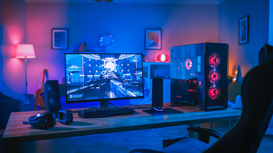 Powerful Personal Computer Gamer Rig With Firstperson Shooter Game On  Screen Monitor Stands On The Table At Home Cozy Room With Modern Design Is  Lit With Pink Neon Light Stock Photo -