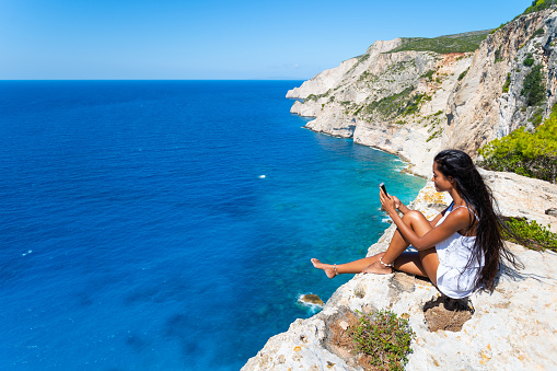 Asian tourist enjoying sea view and using smart phone in Zakynthos Greece - Navagio beach