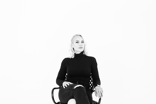 Black and white studio portrait of an attractive blond woman in a black turtleneck jumper against plain background