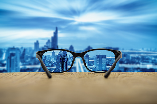 Clear cityscape focused in glasses lenses with blurred cityscape background.