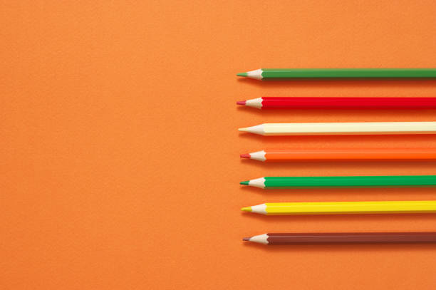 Colorful pencils as border on textured orange paper as background. Top view, flat lay.