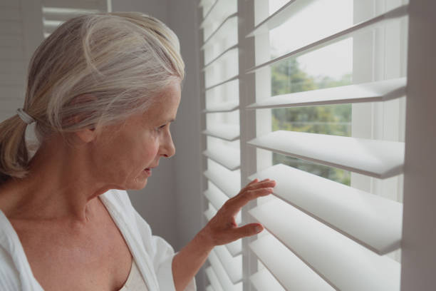 istock Active senior woman looking through window in a comfortable home 1157297075