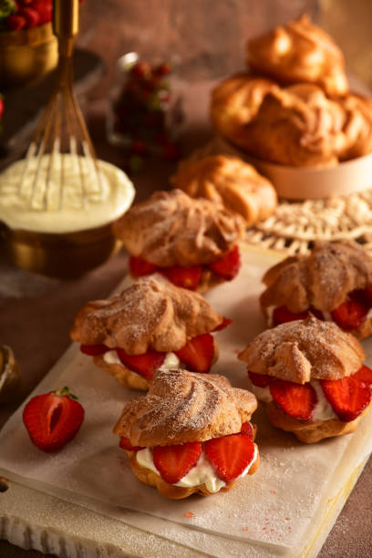 istock Eclairs custard cakes (shu, profiteroles) with strawberries on a dark background. Still life. 1157298020