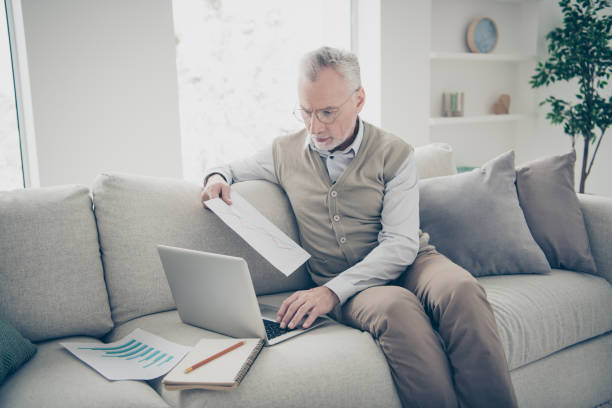 istock Close up side profile photo amazing he him his aged man hand arm notebook search analyzer check information charts stats wear white shirt waistcoat pants sit cozy divan flat house living room indoors 1157298159