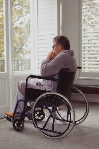 快適な家の車椅子の窓を通して見ている障害者アクティブシニア男性 - healthcare and medicine home interior side view vertical ストックフォトと画像