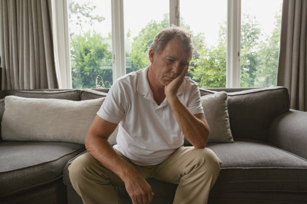 istock Active senior man with hand on face sitting on sofa in a comfortable home 1157311142