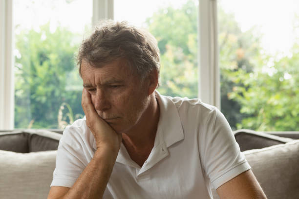 istock Active senior man with hand on face sitting on sofa in a comfortable home 1157311186