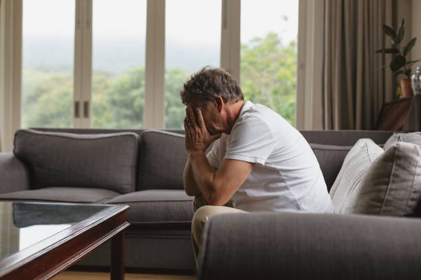 istock Active senior man covering his face with hands while sitting on sofa in a comfortable home 1157312023