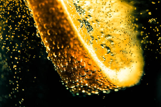 Extreme close up macro color image depicting a slice of lemon in a carbonated drink with many bubbles as the lemon has just been dropped into the drink. Dark background with room for copy space.