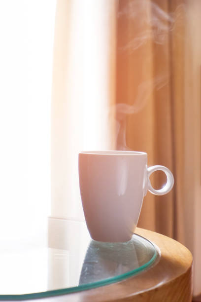 istock One cup hot coffee with smoke on the glass table in the window light in room. 1157314063