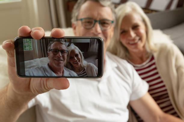 istock Active senior couple sitting on sofa and taking selfie in a comfortable home 1157316456
