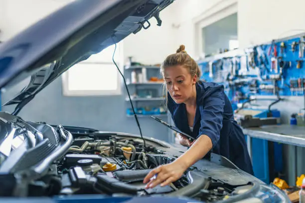 Photo of Lovely female auto mechanic, examining engine of an automobile