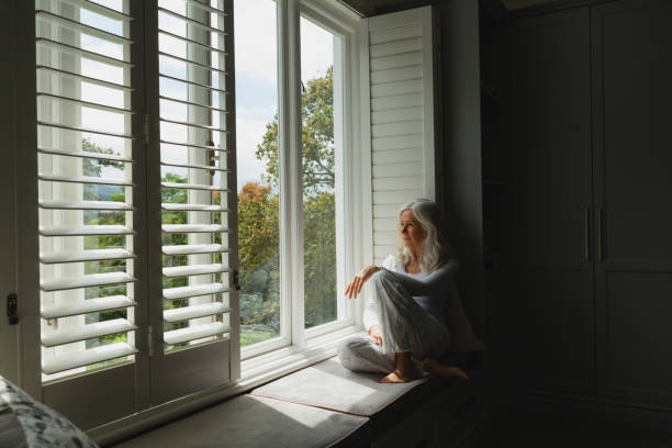 istock Active senior woman looking through window at home 1157319514