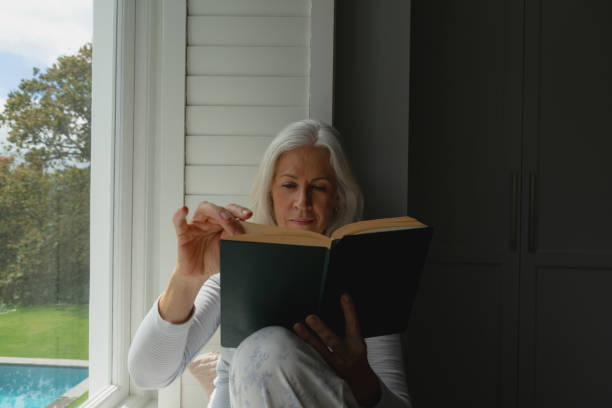 istock Active senior woman reading a book on window seat 1157319821