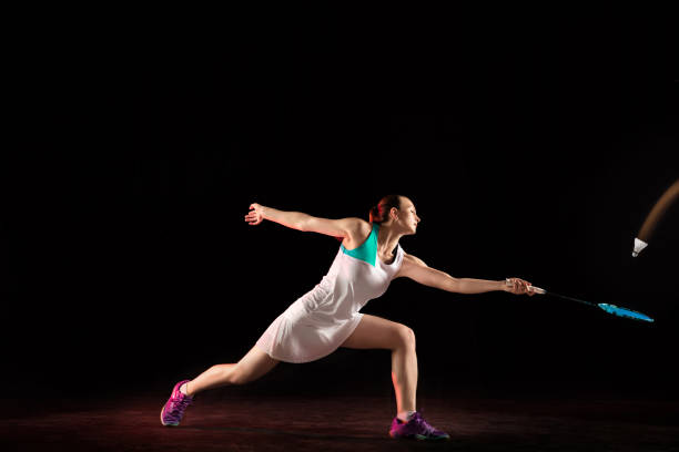 Young woman playing badminton isolated on black background in neon light. Female model with the racket in action, motion in game with the shadows. Concept of sport, movement, healthy lifestyle.