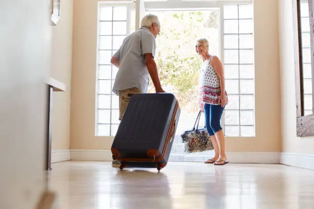 Photo of Senior Couple Standing By Front Door With Suitcase About To Leave For Vacation