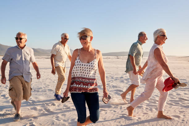 istock Group Of Senior Friends Walking Along Sandy Beach On Summer Group Vacation 1157323630