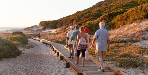 Photo of Group Of Senior Friends Walking Along Boardwalk At Beach On Summer Group Vacation