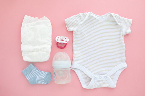 Set for a newborn nipple bottle diaper socks baby body slip pink background top view
